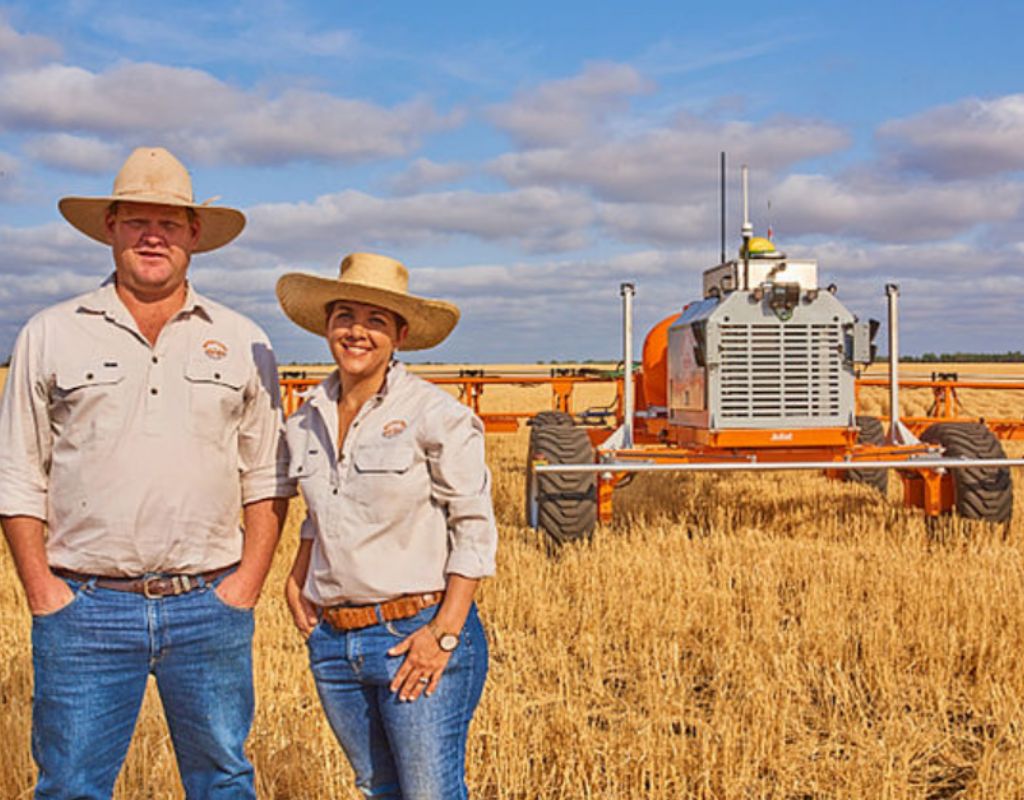 SwarmFarm Robotics founders stand in front of the autonomous tracker they invented in a field of crop